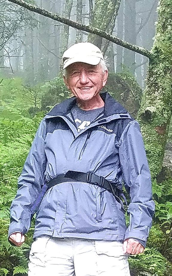 Man in blue jacket and cap smiles while hiking in a misty forest.