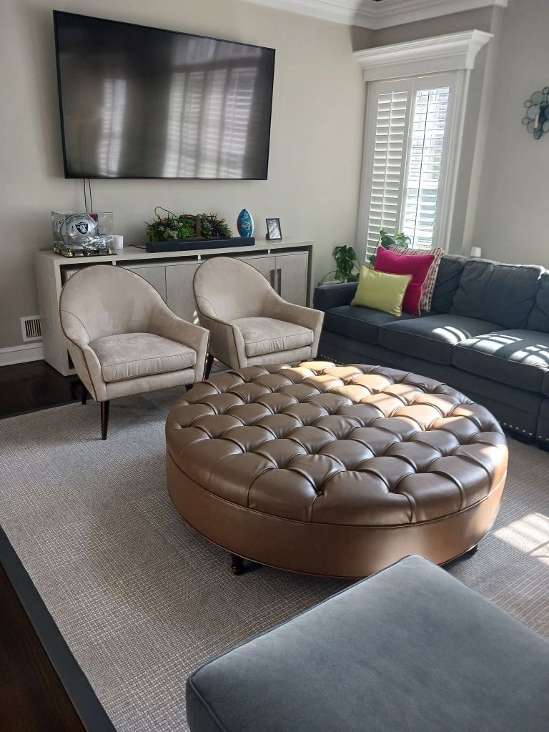 Cozy living room with beige chairs, tufted ottoman, gray sofa, and wall-mounted TV