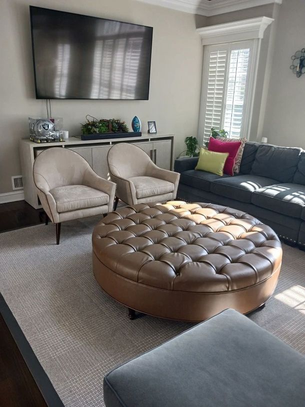 Cozy living room with beige chairs, tufted ottoman, gray sofa, and wall-mounted TV