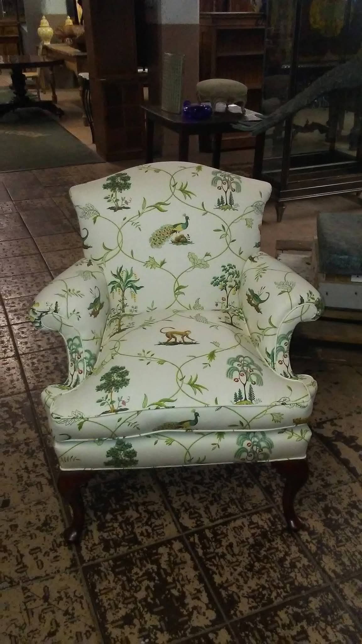 White floral armchair with green pattern in a dimly lit indoor room, on a patterned rug.