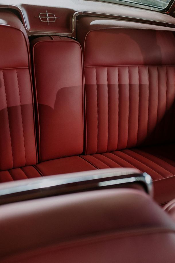 Red leather car back seat with vertical stitching and chrome trim inside a vintage interior