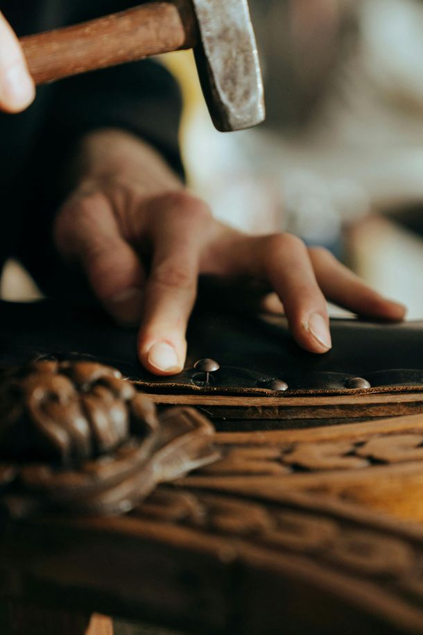 Hand using a hammer to tap a nail into a carved wooden surface