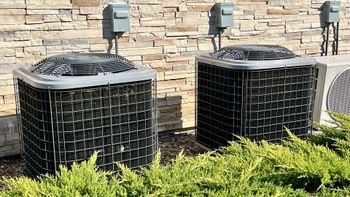 Two air conditioners are sitting next to each other in front of a brick wall.