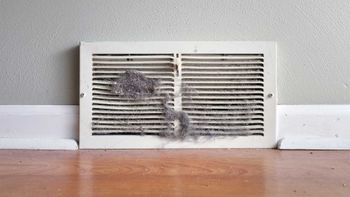 A dirty air vent is sitting on a wooden floor next to a wall.