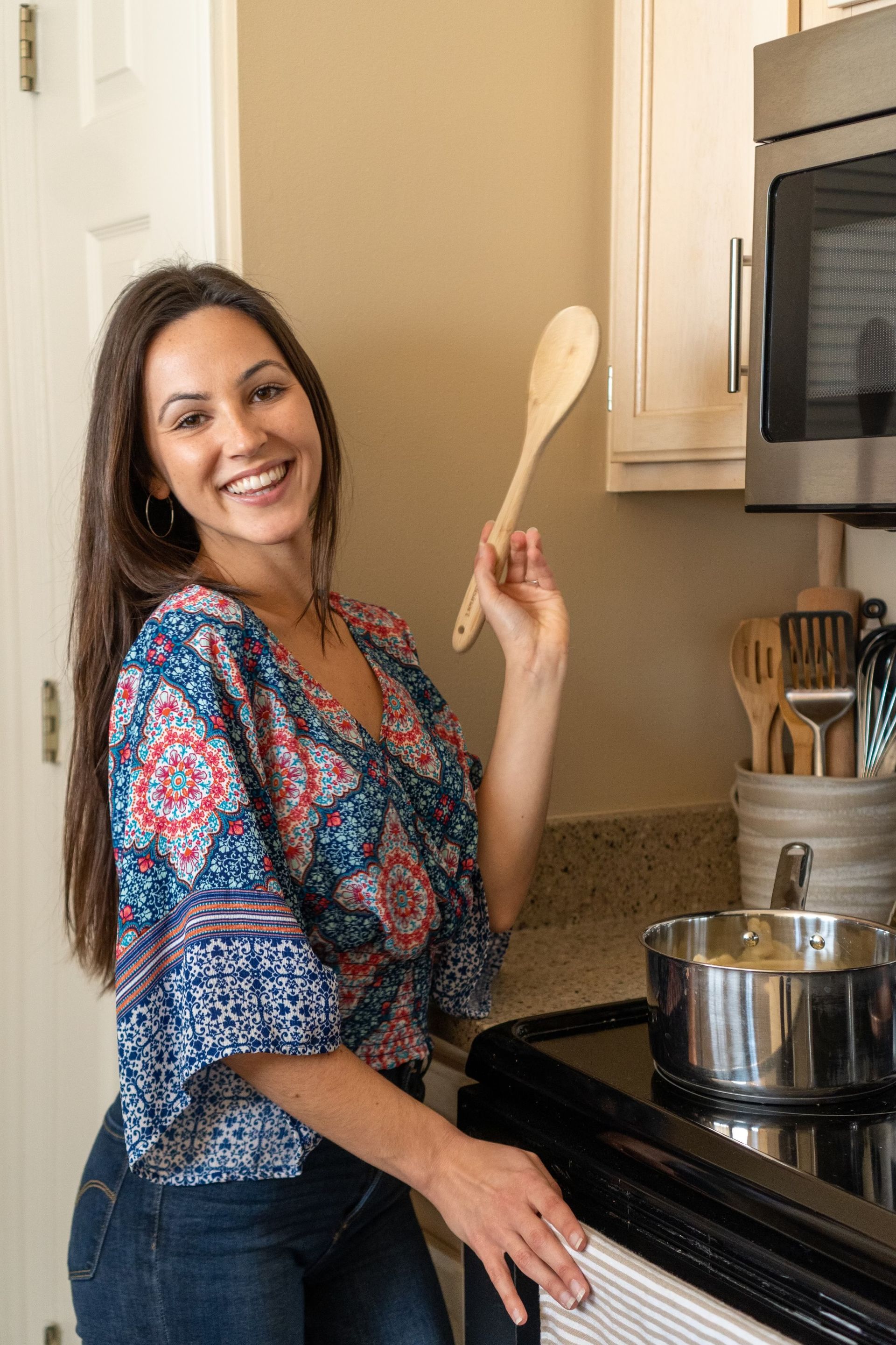 A woman is standing in a kitchen holding a wooden spoon.