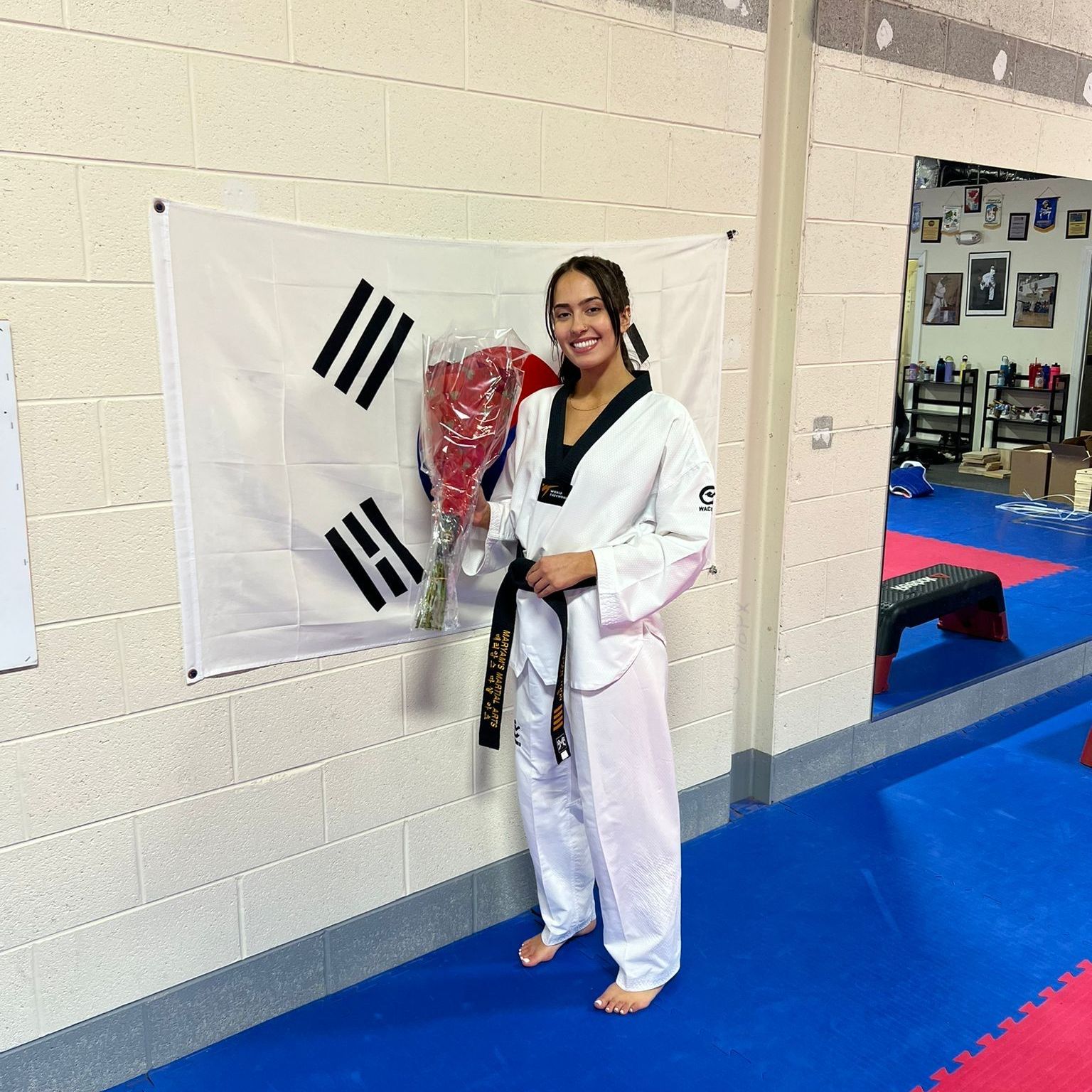 A woman in a taekwondo uniform is holding a bouquet of flowers