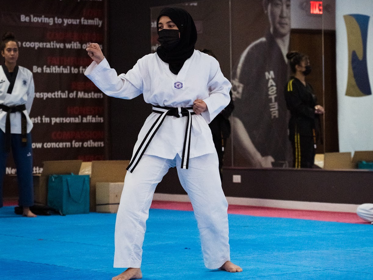 A woman in a hijab is practicing martial arts on a blue mat