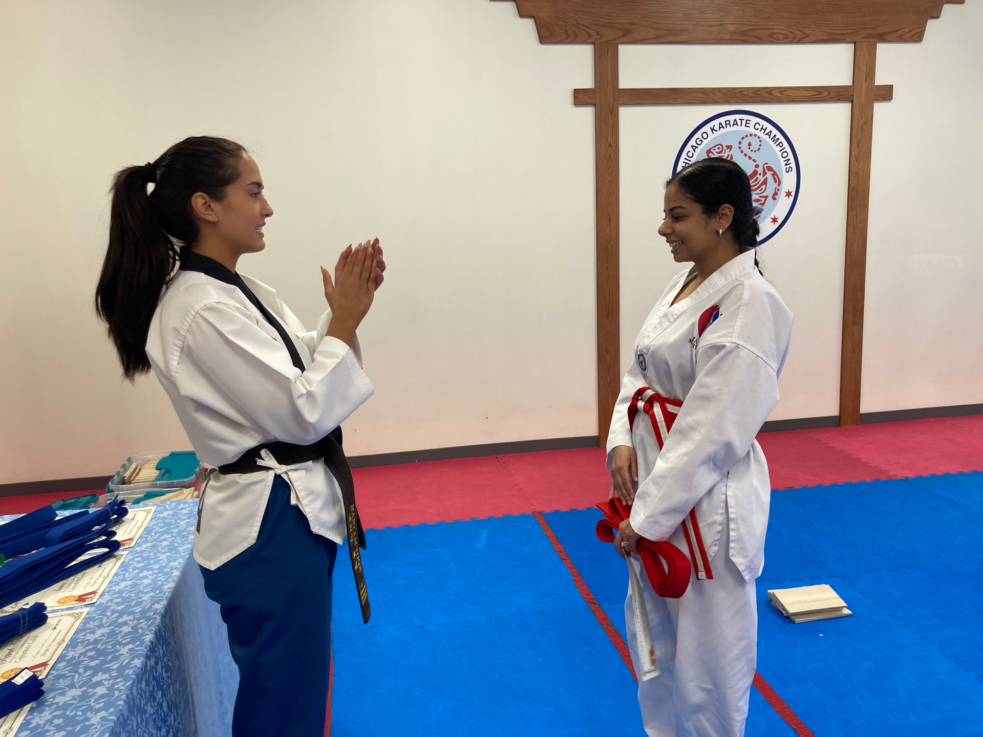 Two women in karate uniforms are standing next to each other on a blue mat.