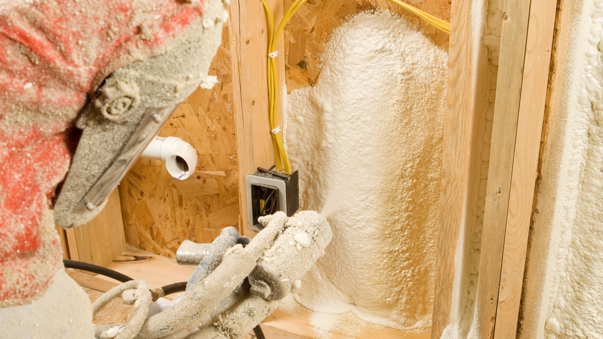 Spray foam insulation being applied to a wall cavity inside a wooden construction frame.