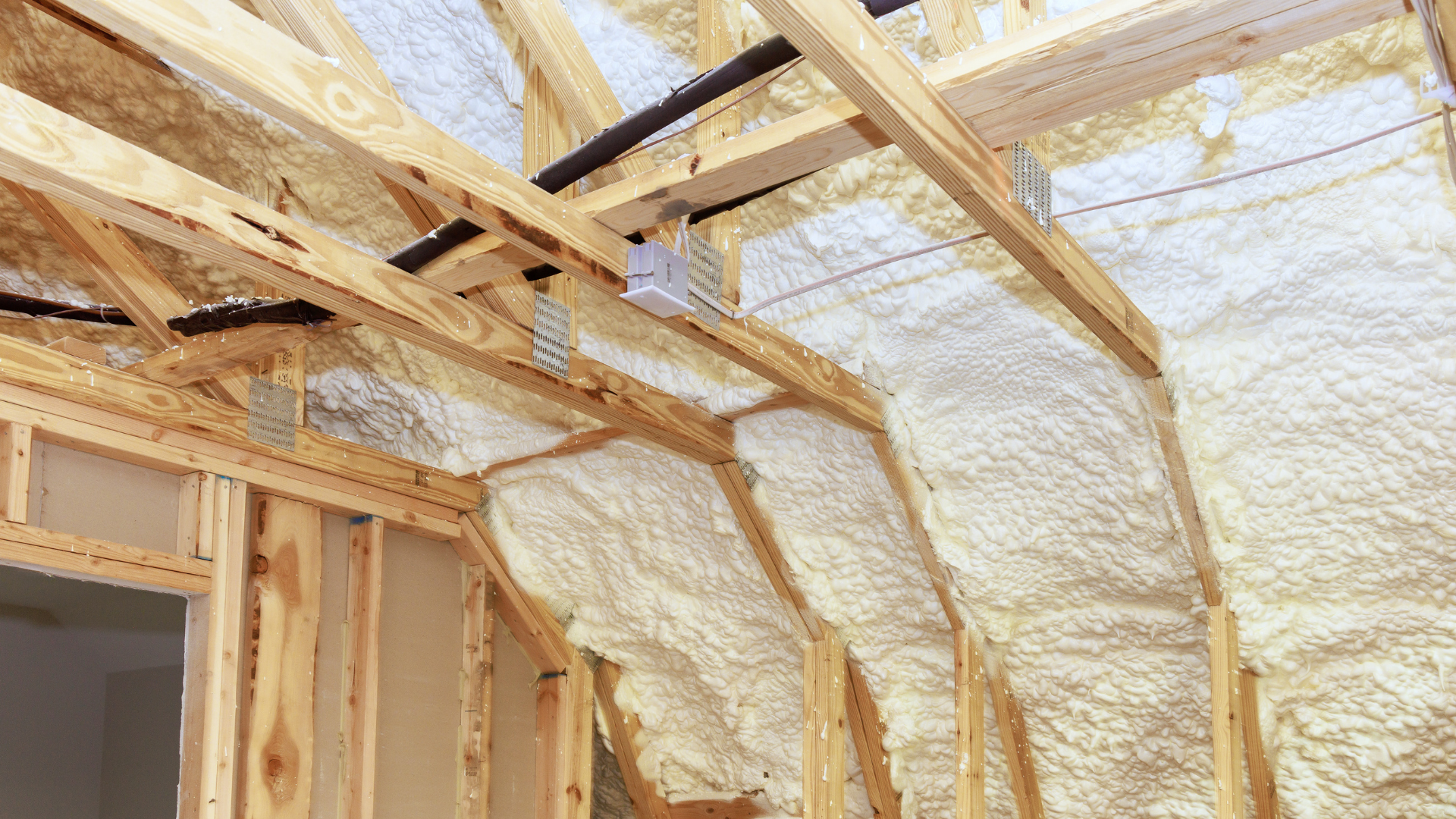 Exposed attic framing with spray foam insulation applied between wooden rafters and studs.