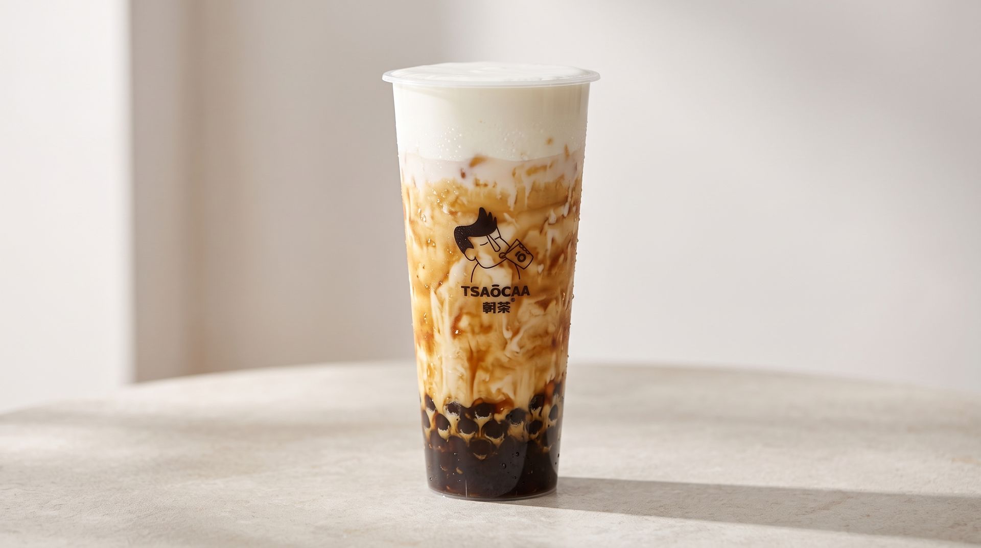 Iced layered brown sugar milk tea in a clear plastic cup on a light table.