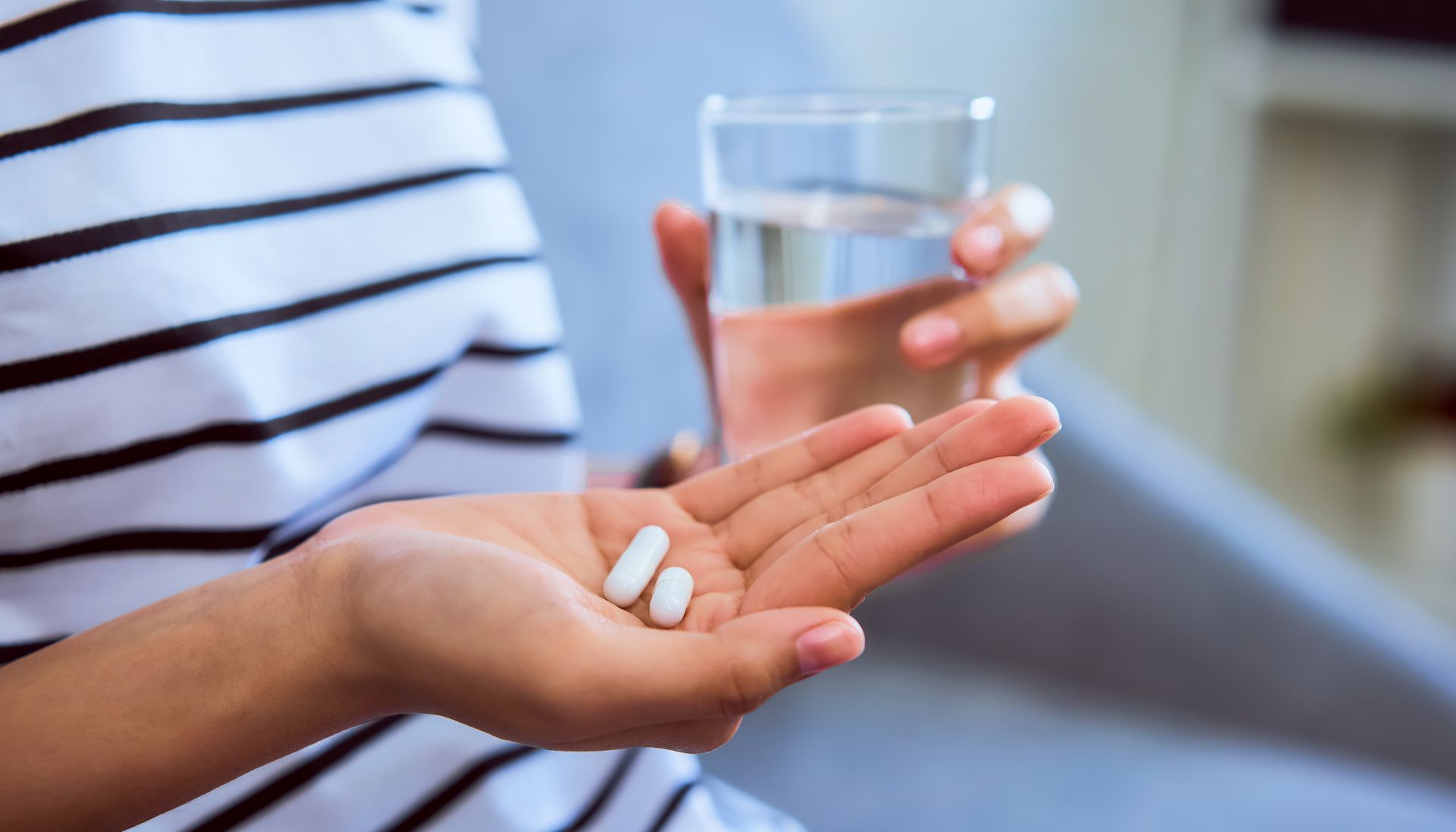 Close-up of hand holding pain medicine tablets and water glass for non-surgical pain care.