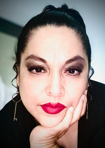 Woman with dark hair in a high bun and dramatic eye makeup, wearing red lipstick, resting chin on hand.