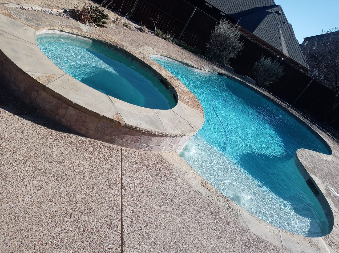 Curved backyard swimming pool with turquoise water and a raised circular hot tub beside it