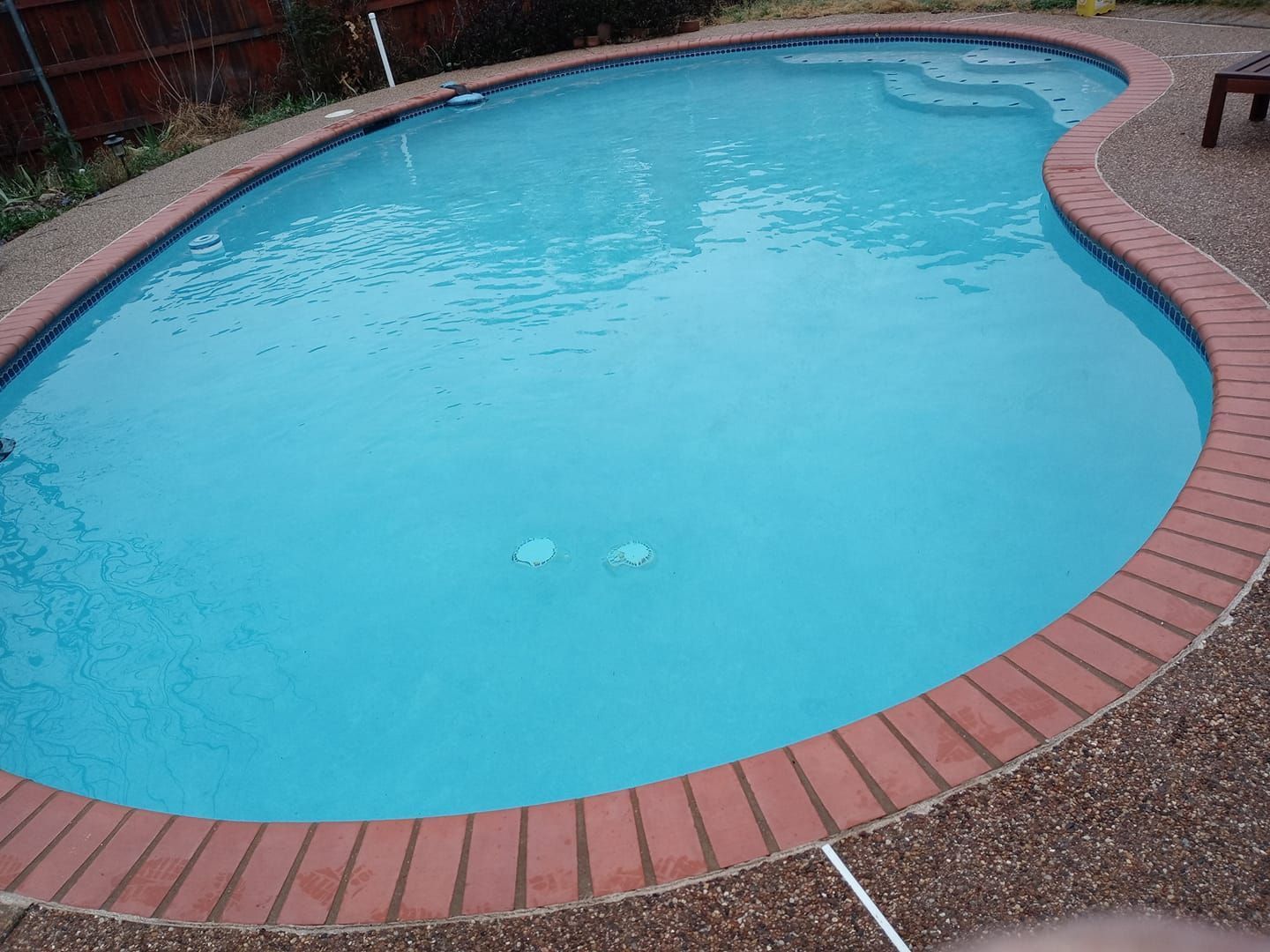 Empty blue swimming pool with red brick coping and gravel deck