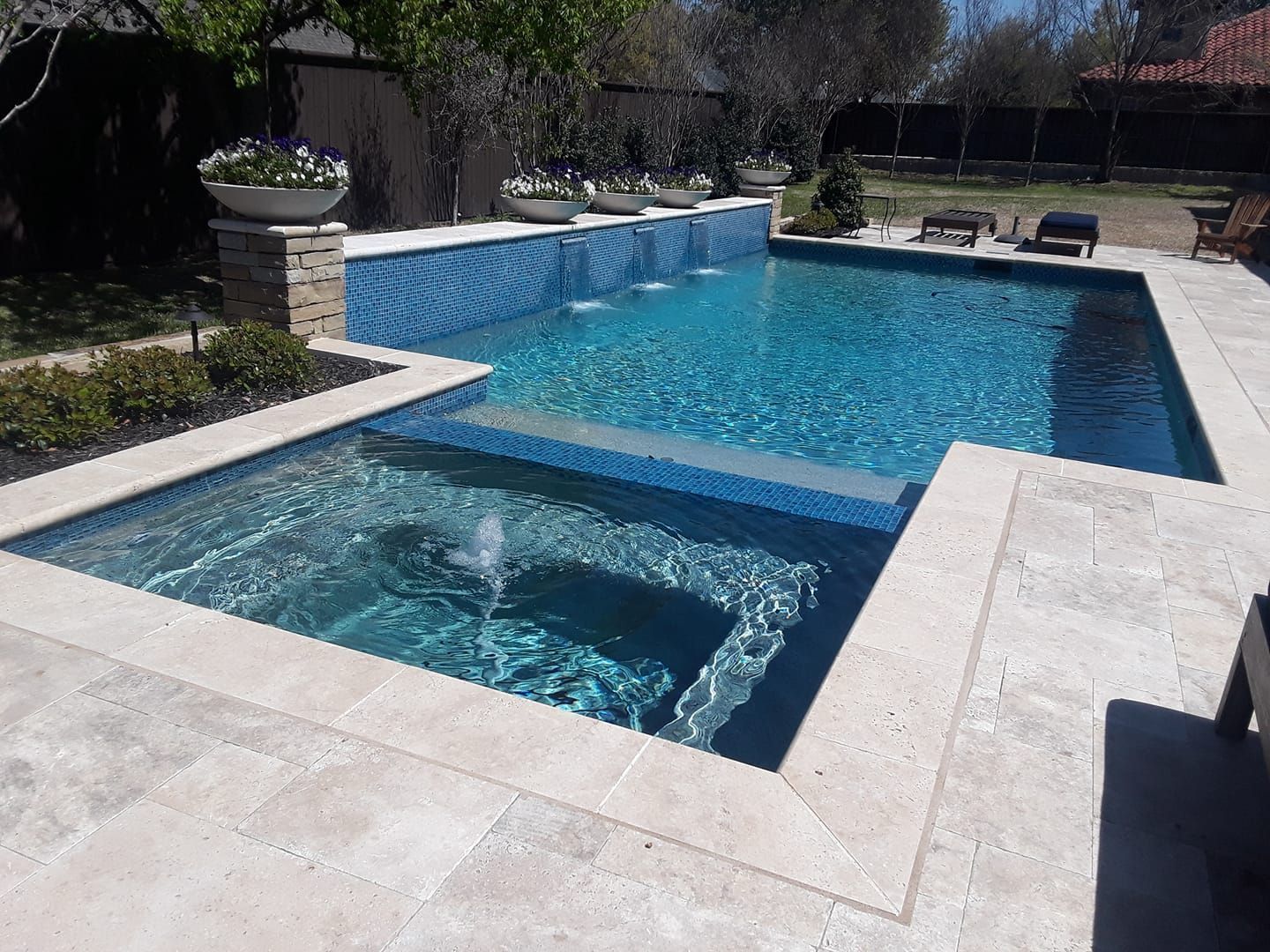 Modern backyard pool with a raised spa and clear blue water, surrounded by light stone decking.