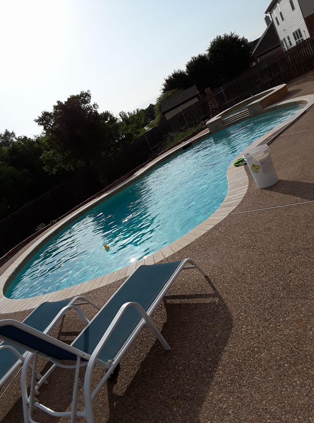 Tilted view of an outdoor swimming pool with lounge chairs and a white deck chair on the patio