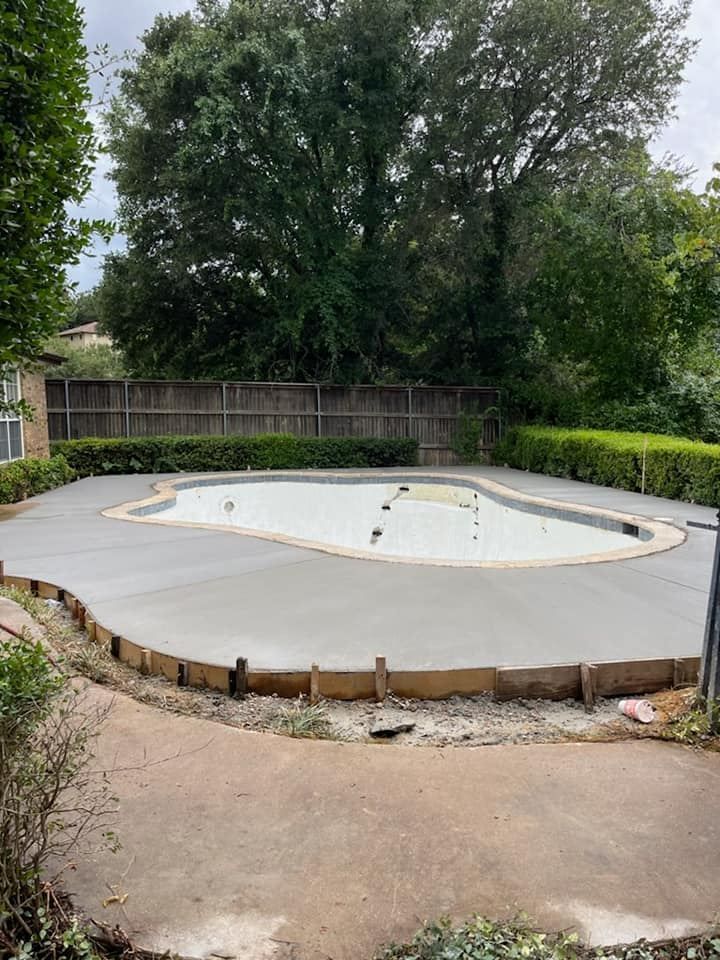 Empty backyard swimming pool surrounded by concrete, fencing, and trees