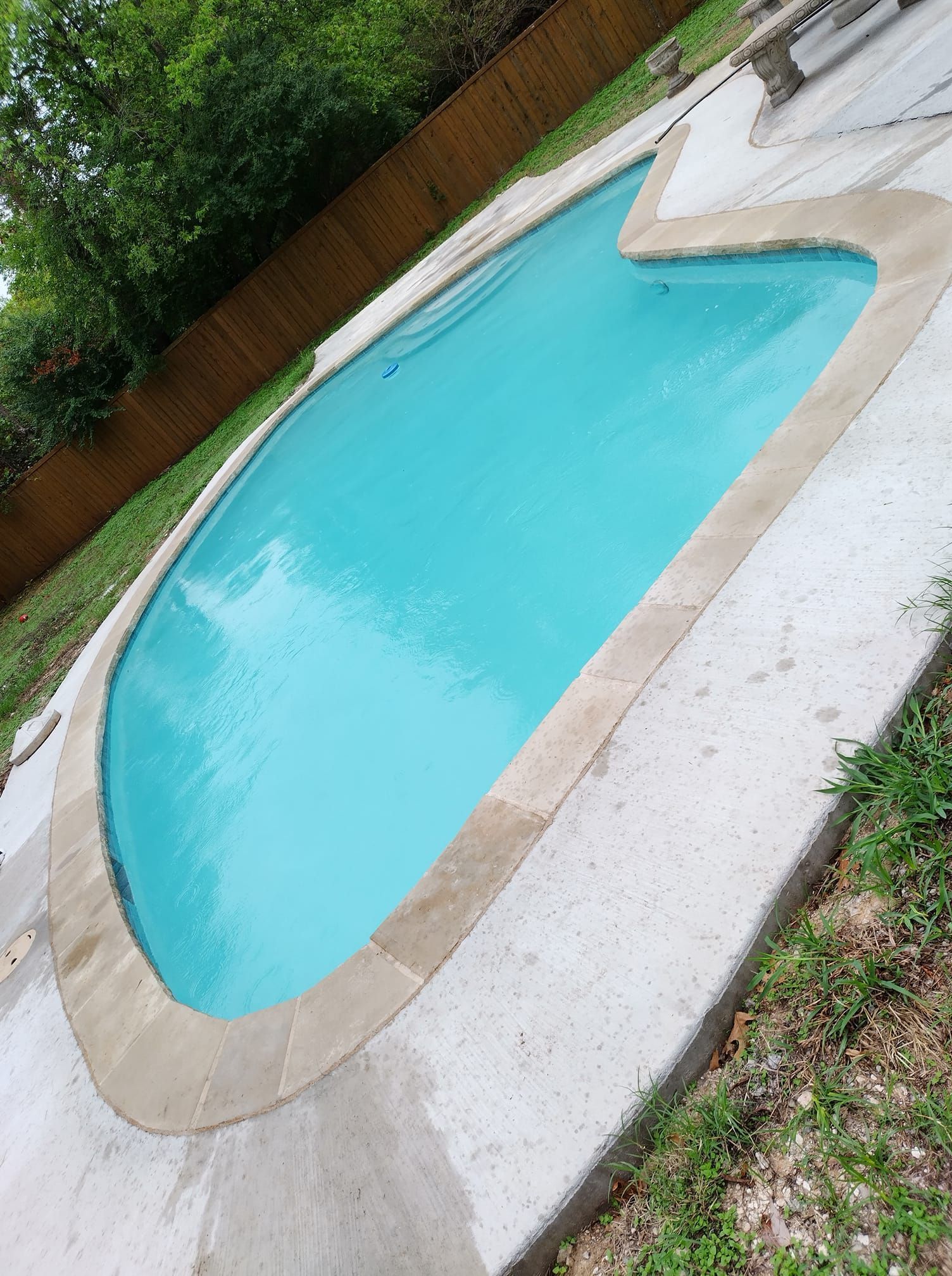 Empty turquoise swimming pool with tan coping and white deck in a backyard