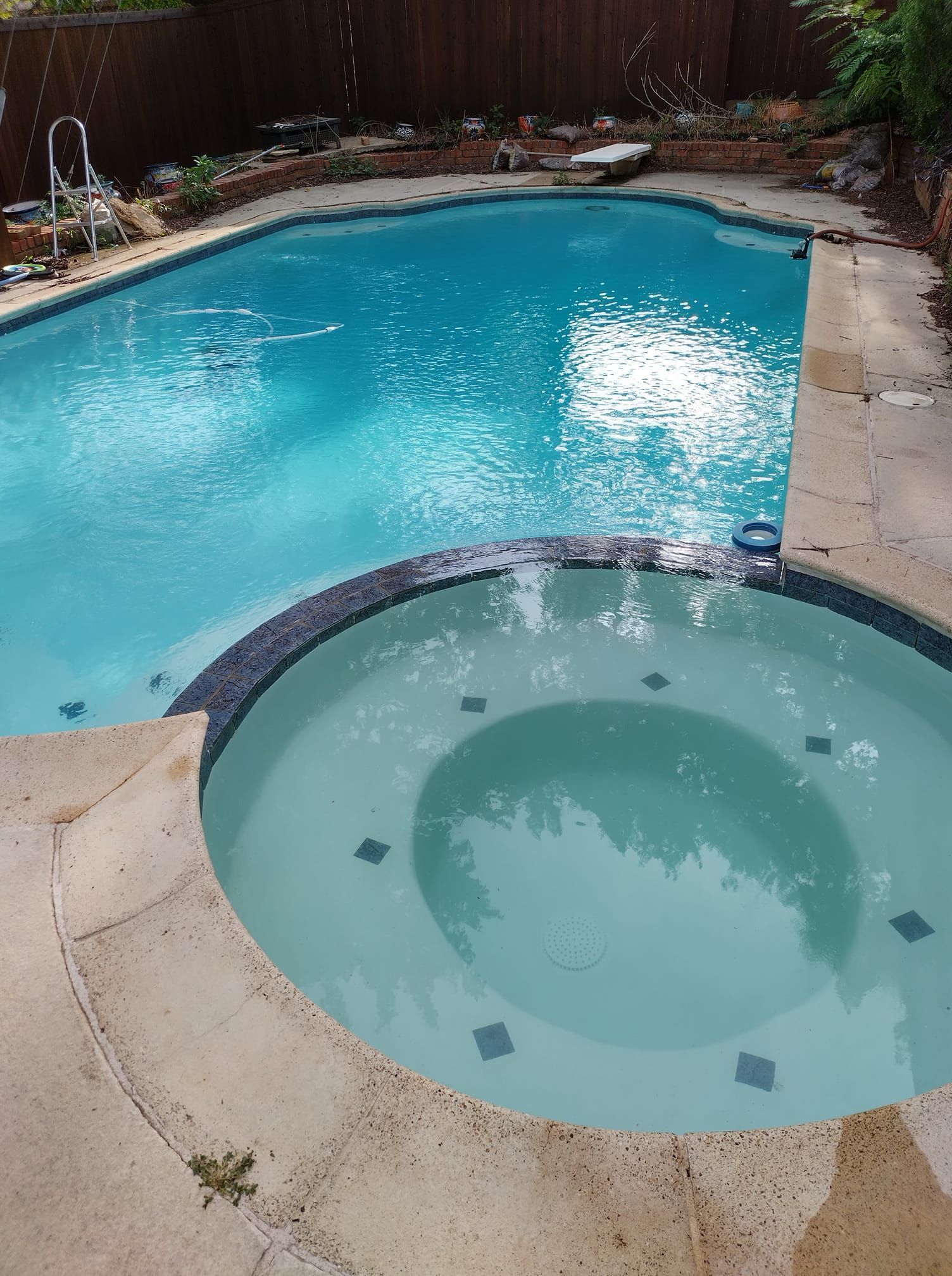 Backyard pool with a circular hot tub, blue water, and beige stone decking