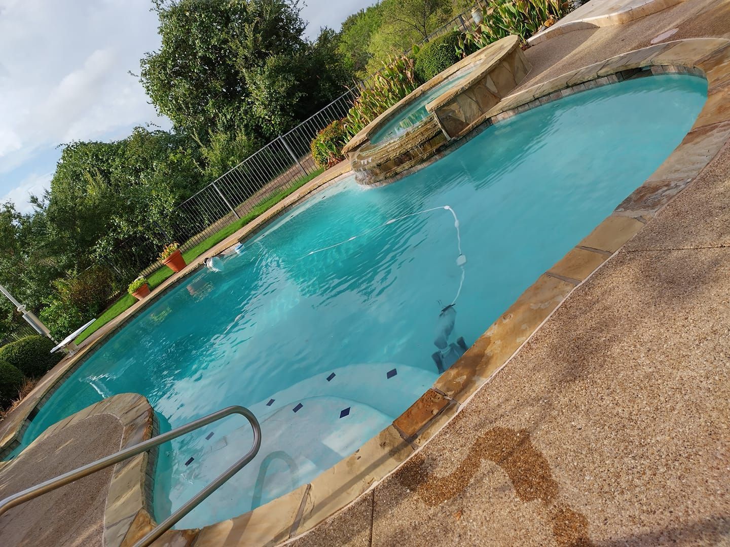 Outdoor swimming pool with turquoise water, concrete deck, ladder, and greenery in the background