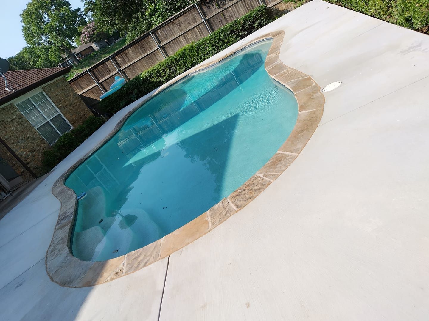Backyard swimming pool with turquoise water and a beige stone border on a white deck