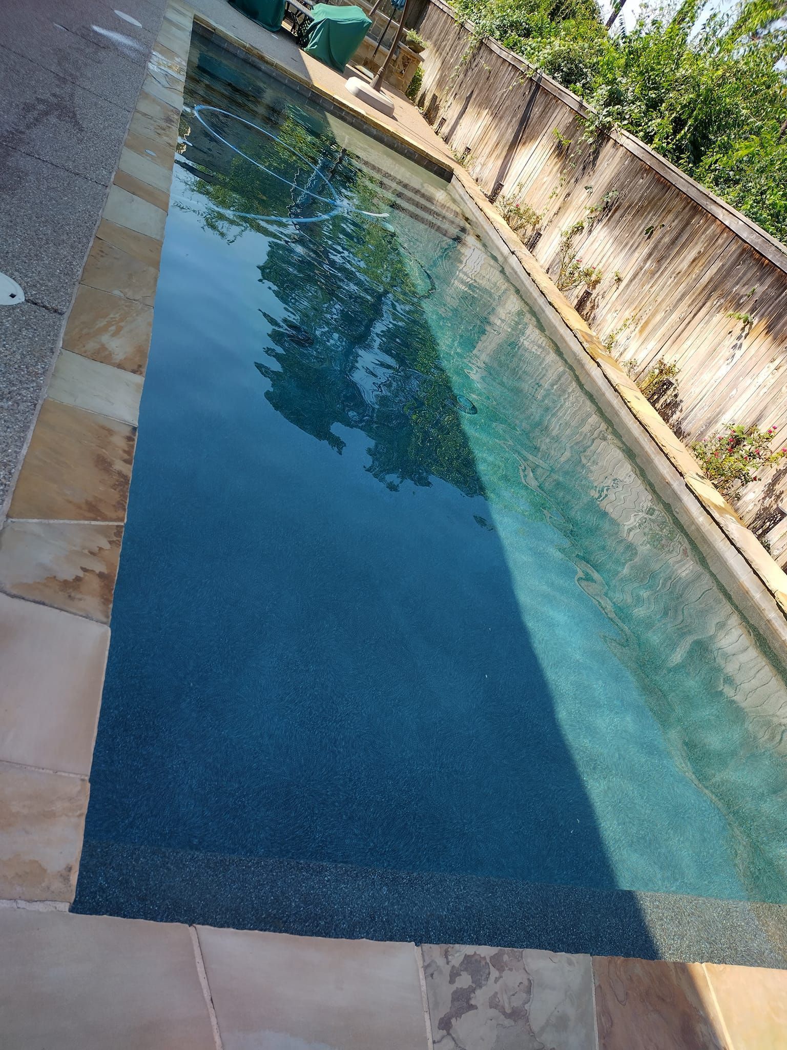 Narrow turquoise swimming pool beside a stone wall, with trees reflected in the water.
