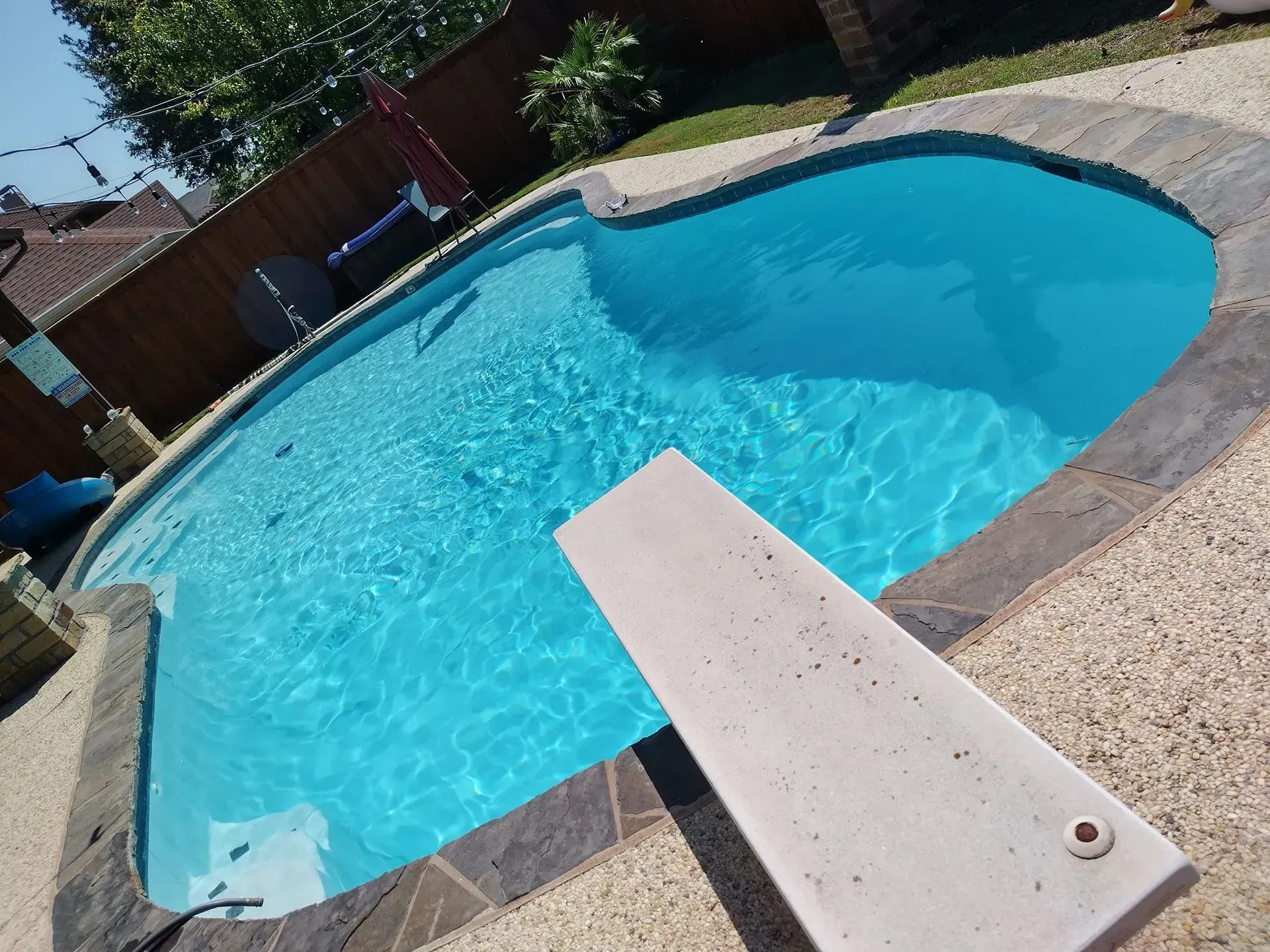 Backyard swimming pool with clear blue water and a diving board on a sunny day