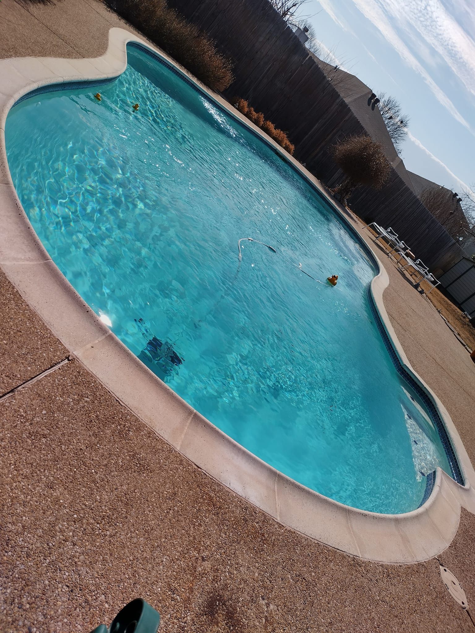 Tilted view of a turquoise backyard swimming pool surrounded by tan decking and a dark fence, with mountains in the distance