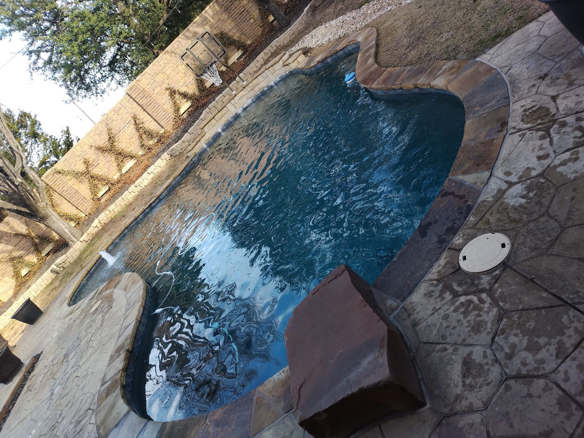Small backyard swimming pool with blue water, stone deck, and a covered lounge chair nearby