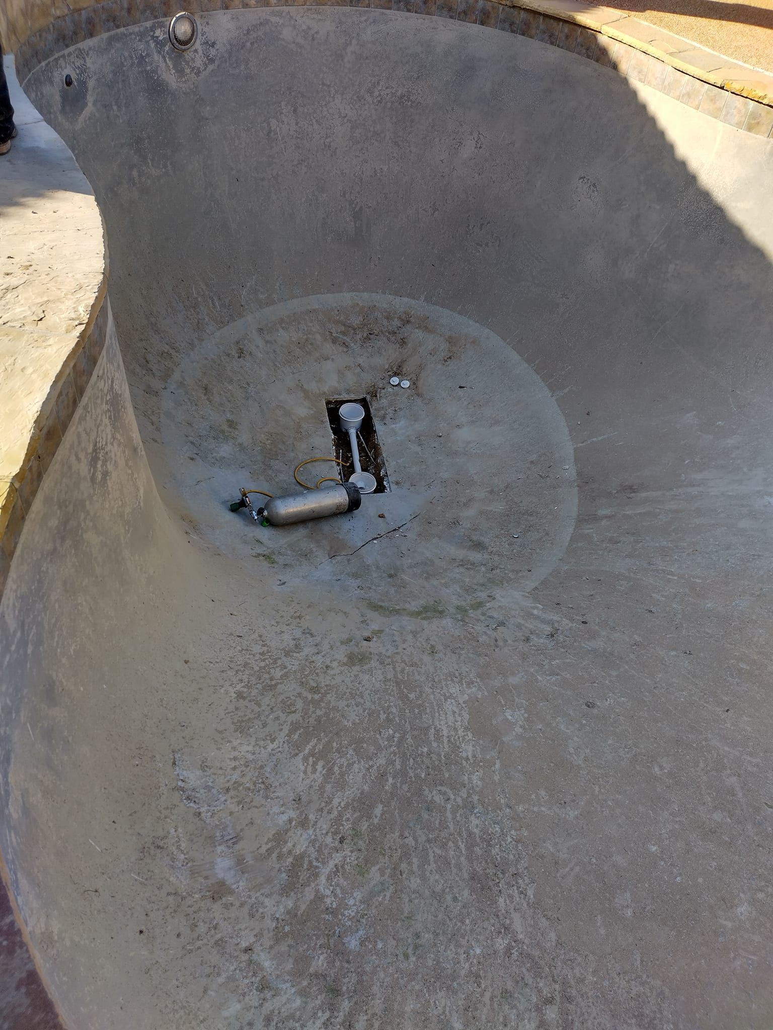 Close-up of a dusty concrete basin with a small black-and-white pipe fitting at the center.
