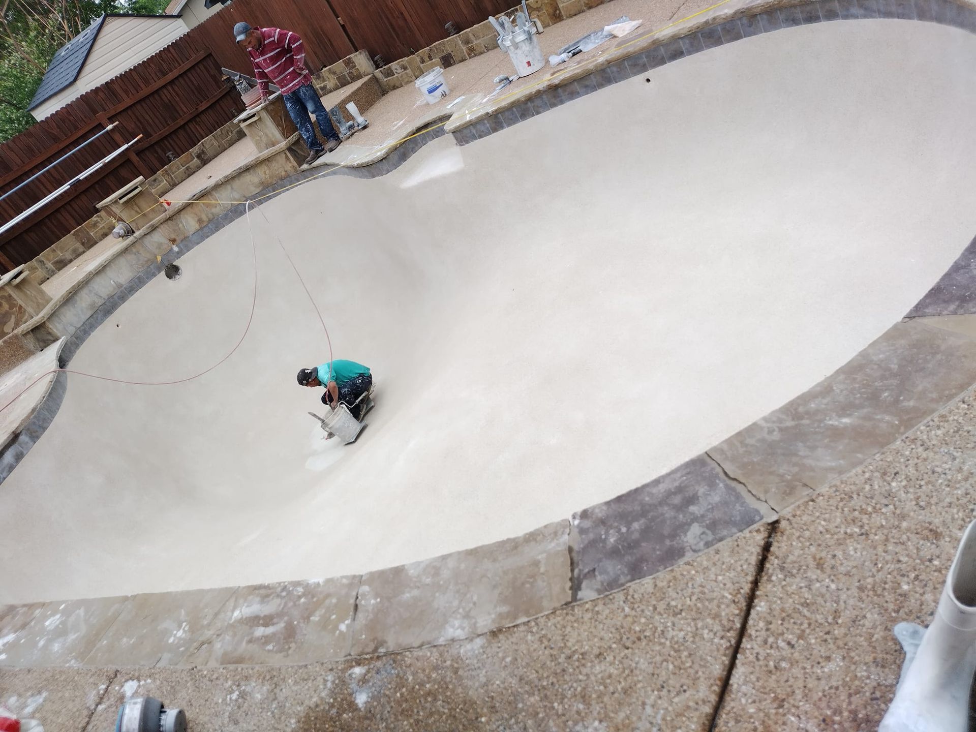Skatepark bowl with a person in a teal shirt riding a skateboard in the center.