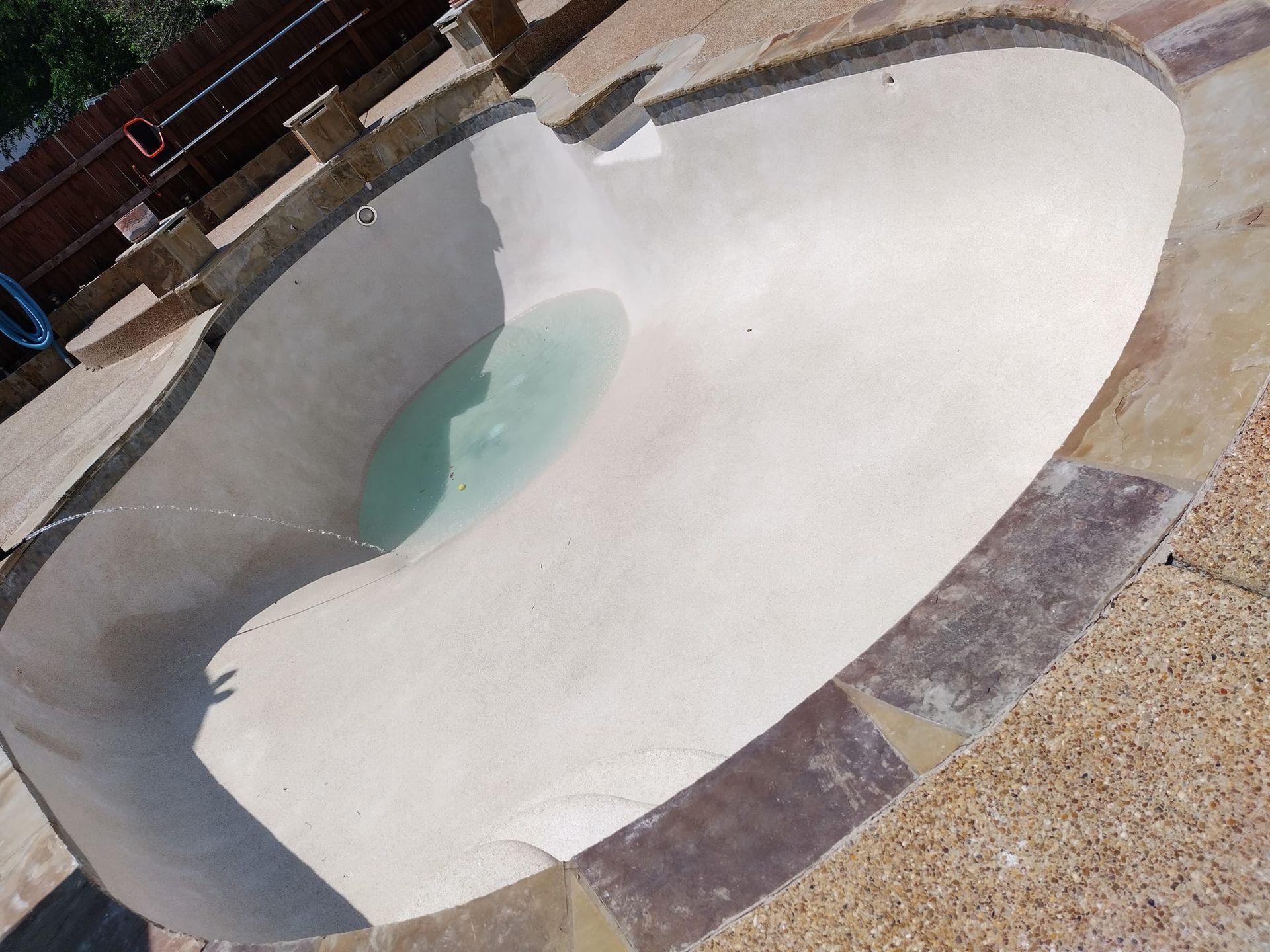 Empty drained swimming pool with a small puddle of greenish water near the edge
