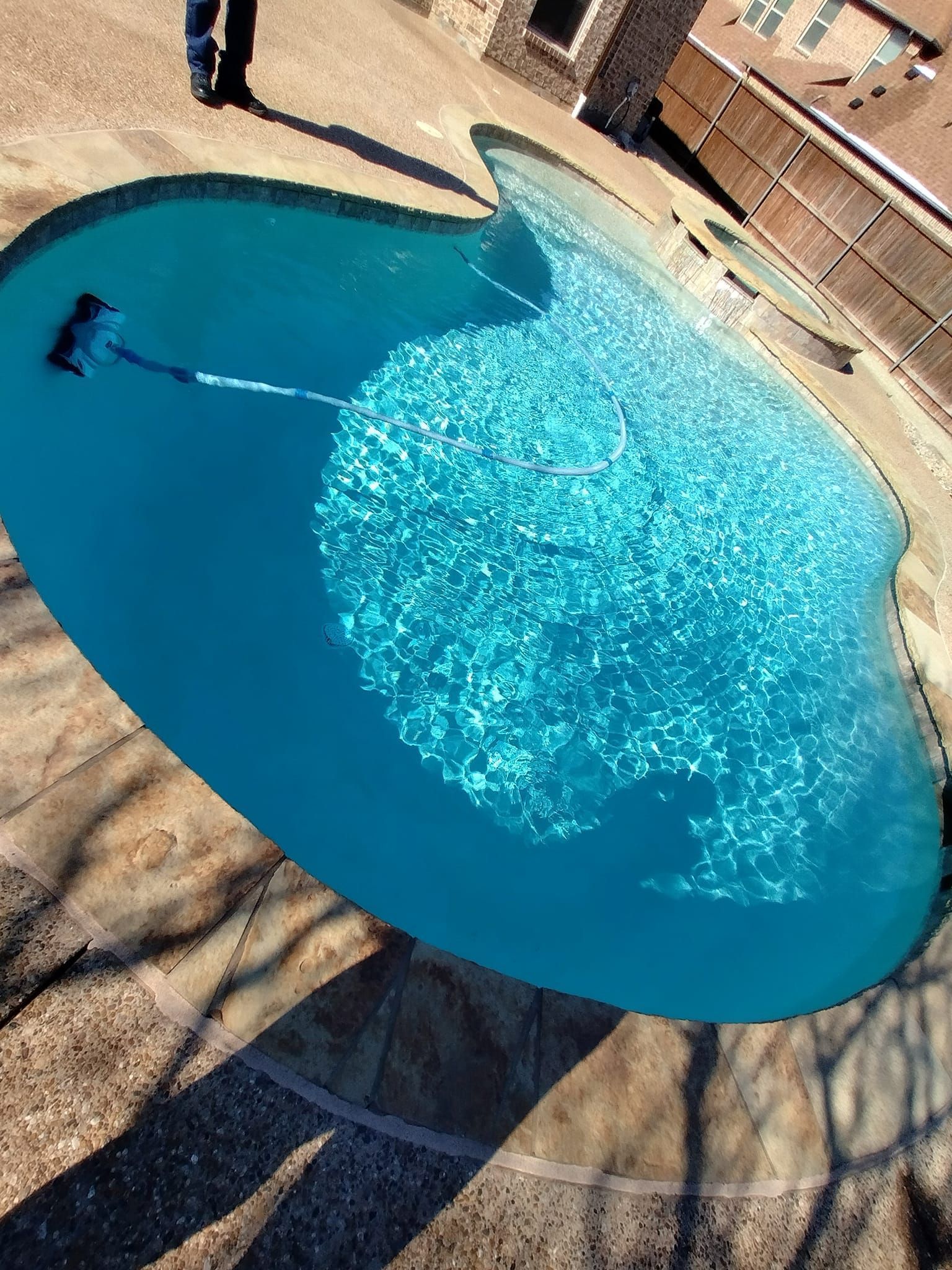 Backyard swimming pool with clear blue water and sunlit ripples, viewed from above