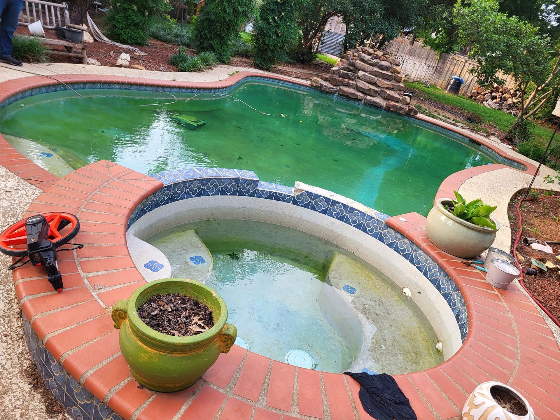 Backyard pool with circular spa, red brick coping, potted plants, and a water fountain spraying into the pool