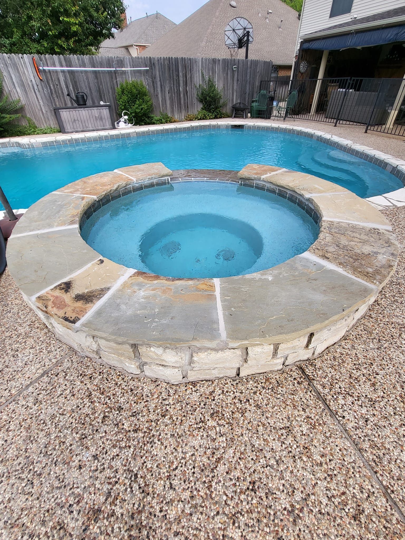Backyard pool with circular hot tub, stone surround, and gravel patio under a clear sky