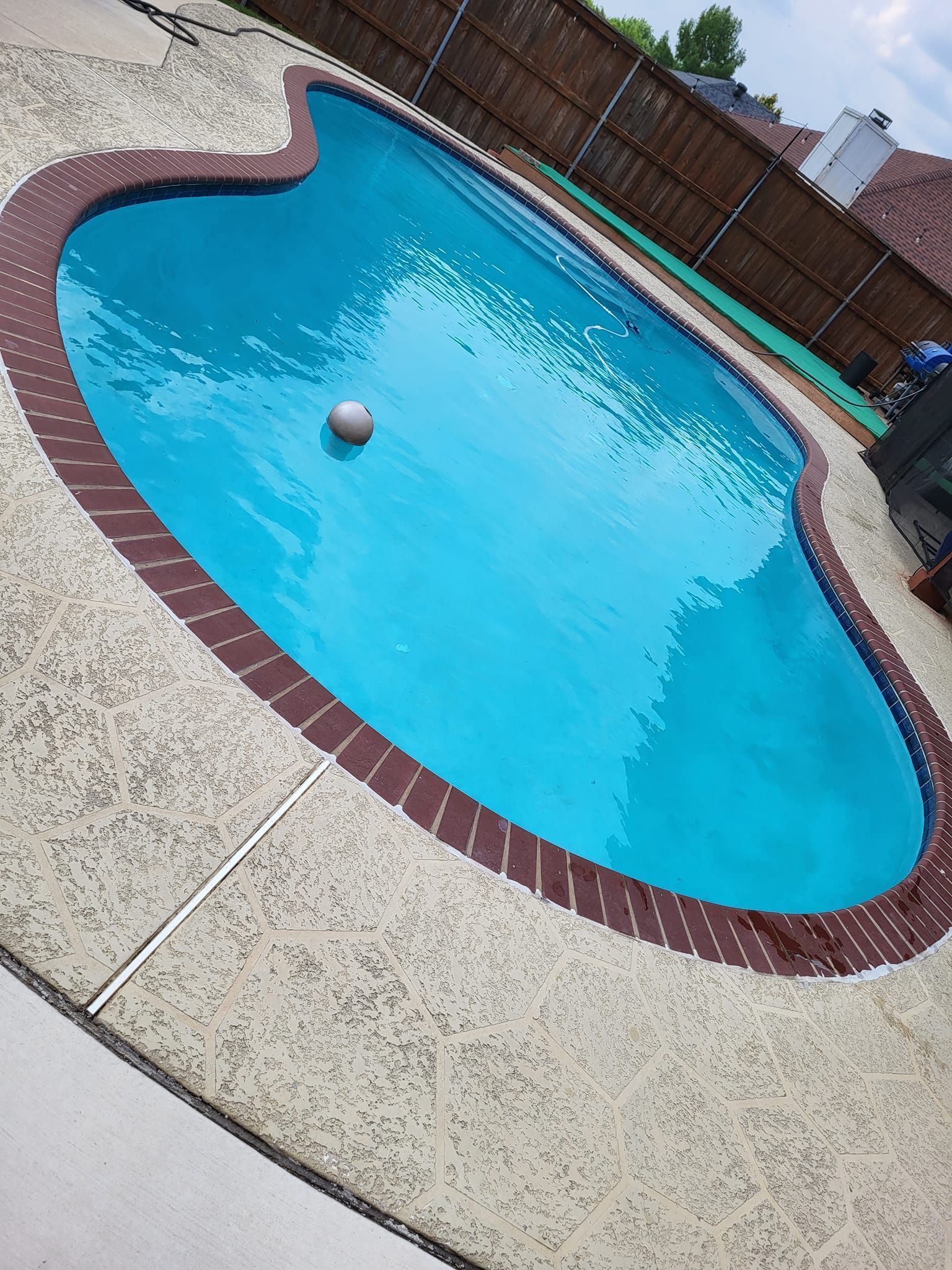 Backyard swimming pool with bright blue water, red brick border, and a floating ball