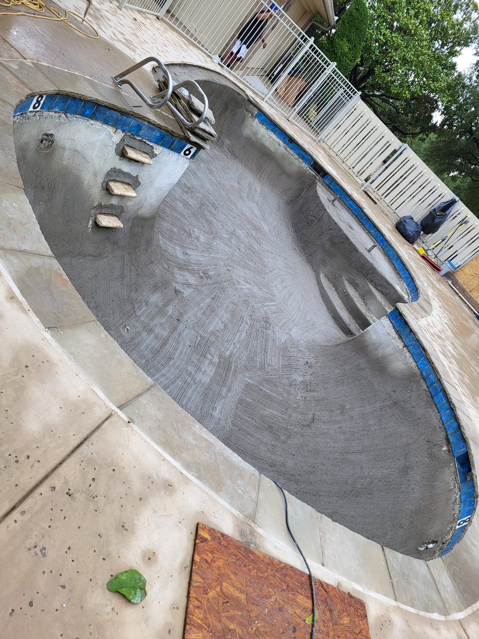 Empty drained swimming pool with a blue-trimmed edge and metal handrail, viewed from above.