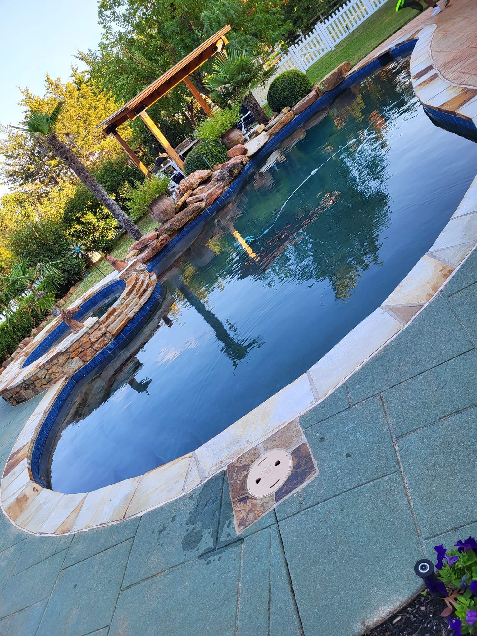 Outdoor swimming pool with blue water, stone edge, and lush greenery reflected on the surface