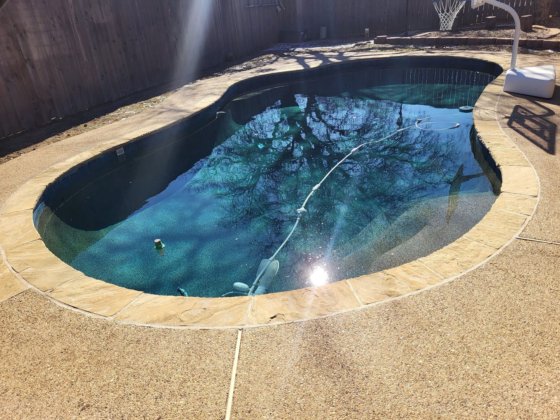 Small backyard swimming pool with blue water, stone deck, and a white hose filling it