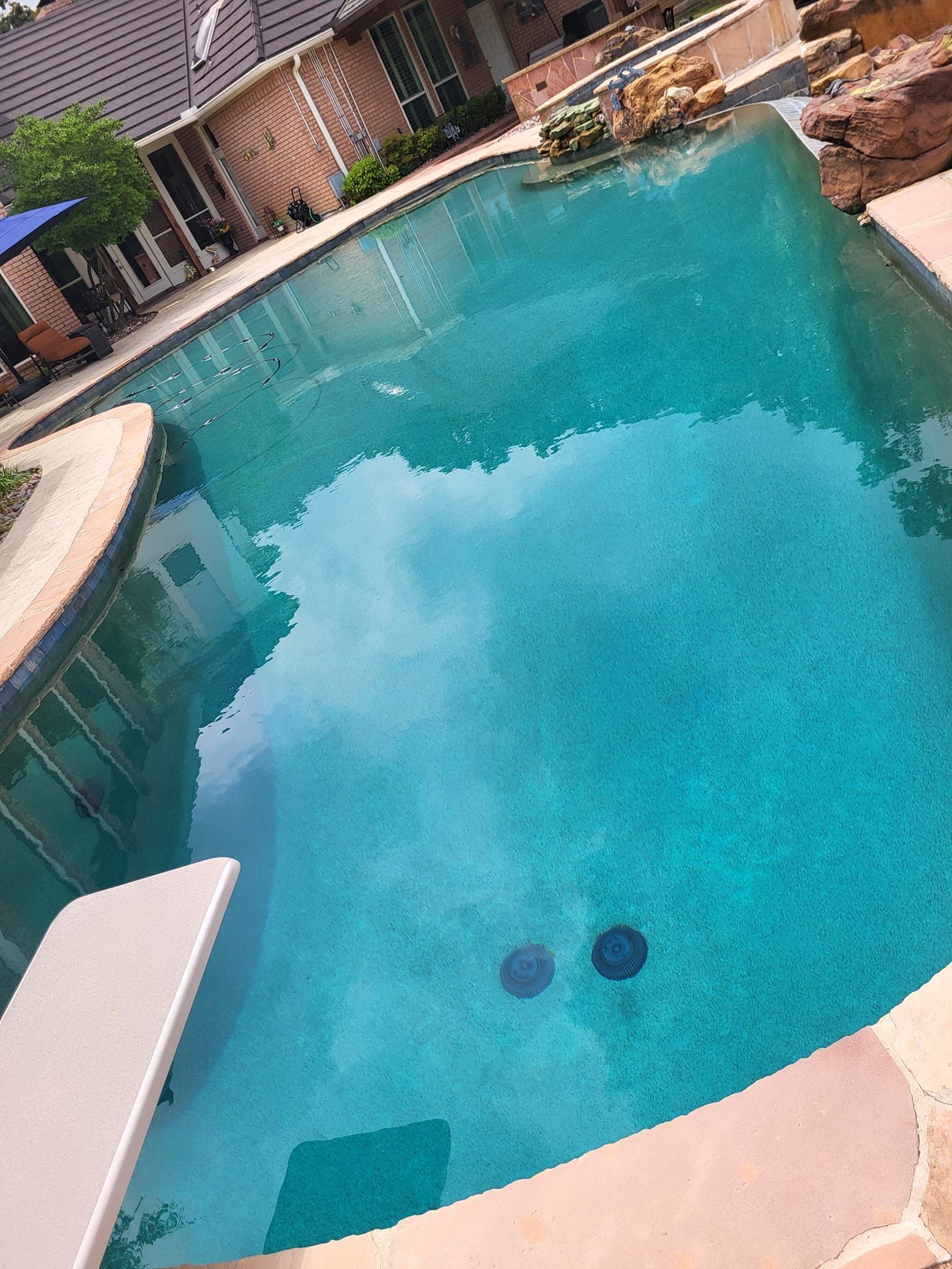 Curved turquoise swimming pool with lounge chairs and a patio in the background