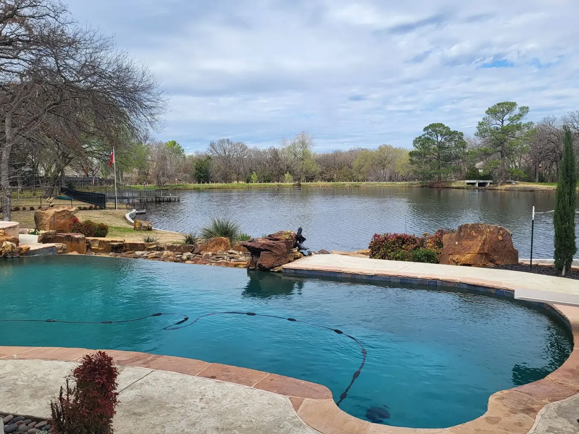 Backyard pool overlooking a calm lake with trees and cloudy sky
