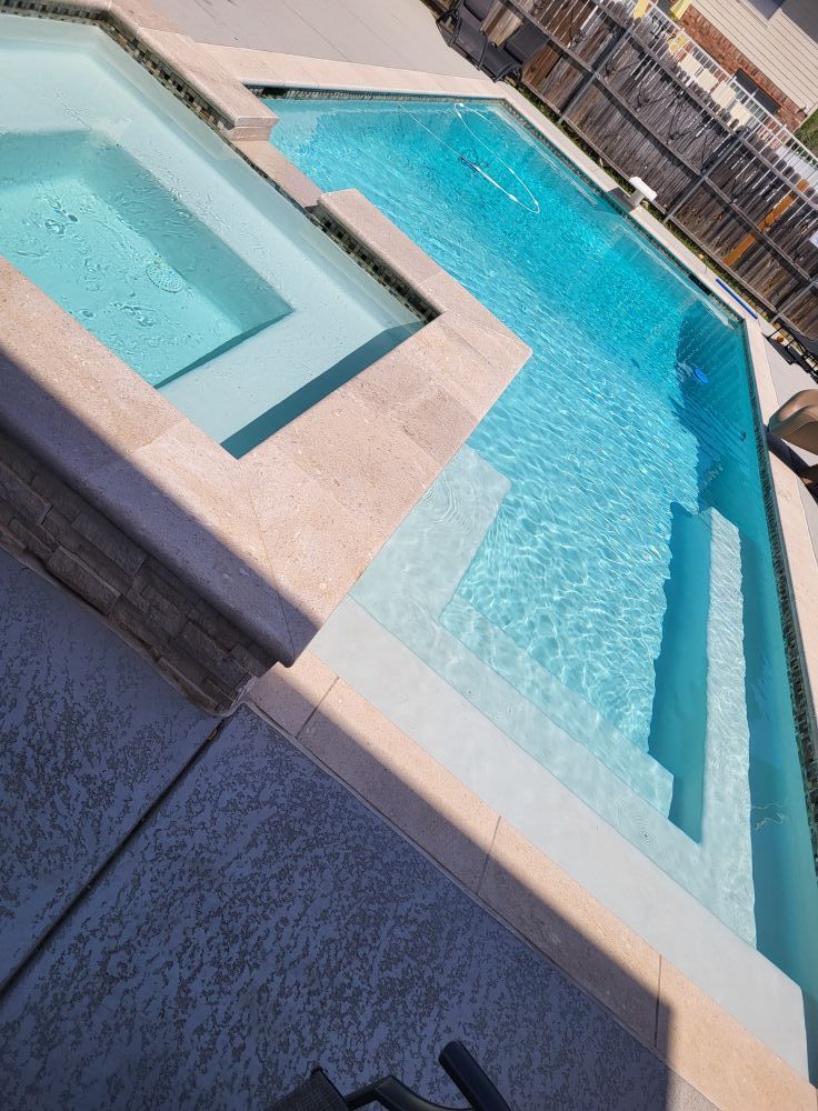 Diagonal view of a turquoise swimming pool with a raised spa and sunlit deck tiles