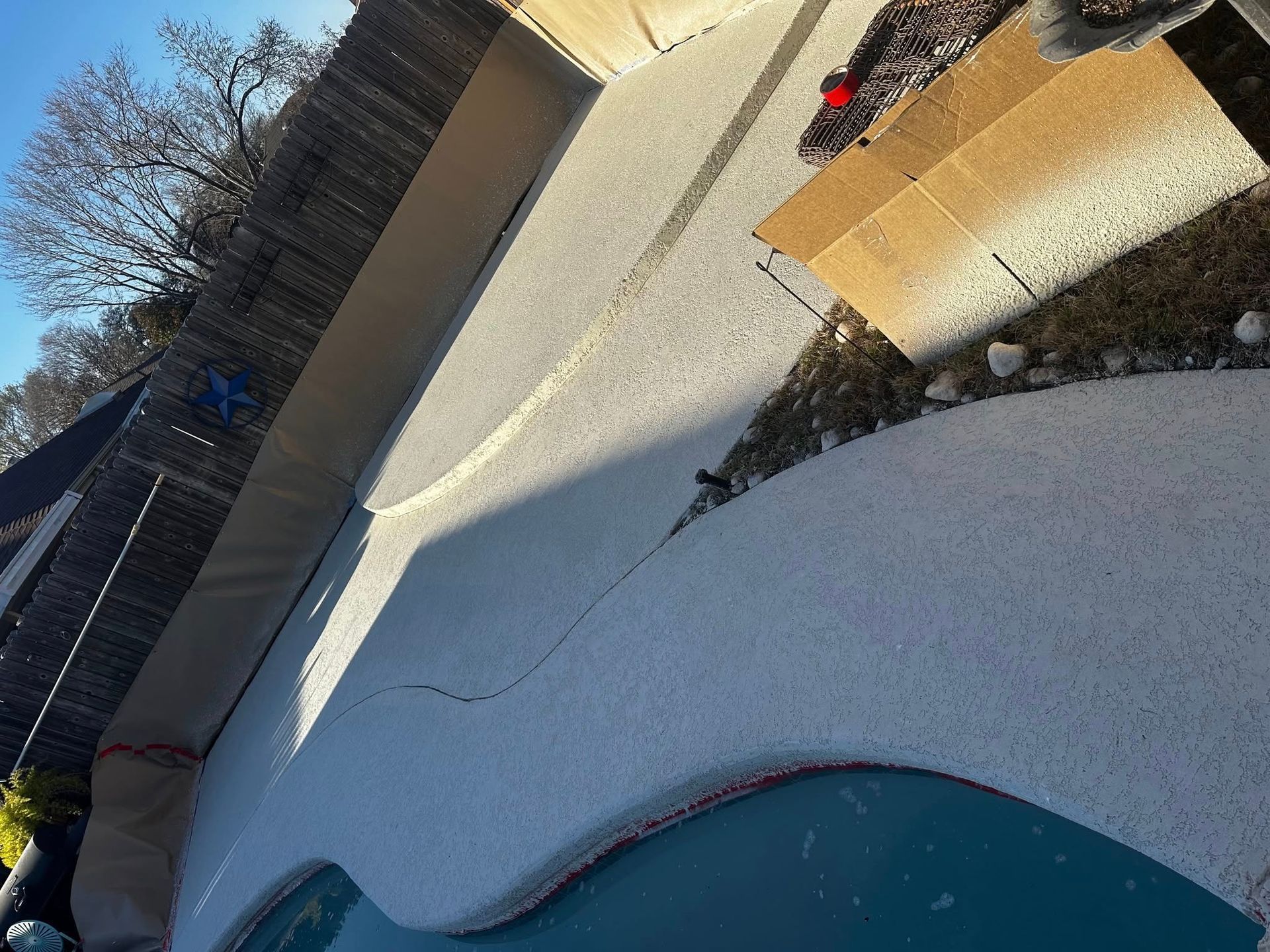 Tilted view of a backyard pool with snowy ground, a fence, and a small wooden deck.