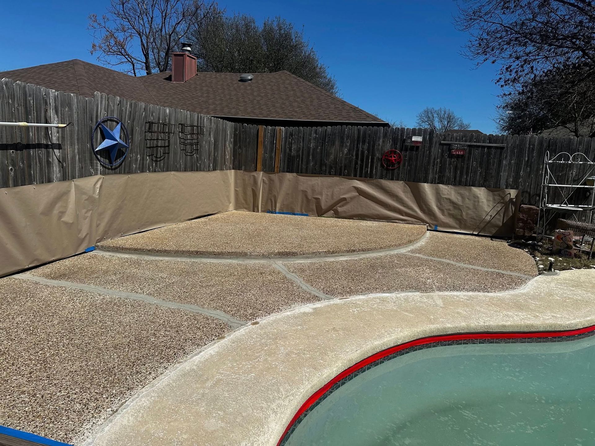 Backyard pool with tan safety barrier and gravel landscaping under a clear blue sky