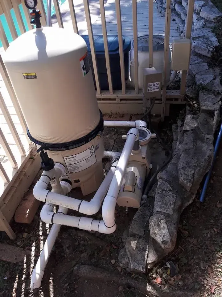 Outdoor pool filter and white PVC pipes beside a fence and stone border