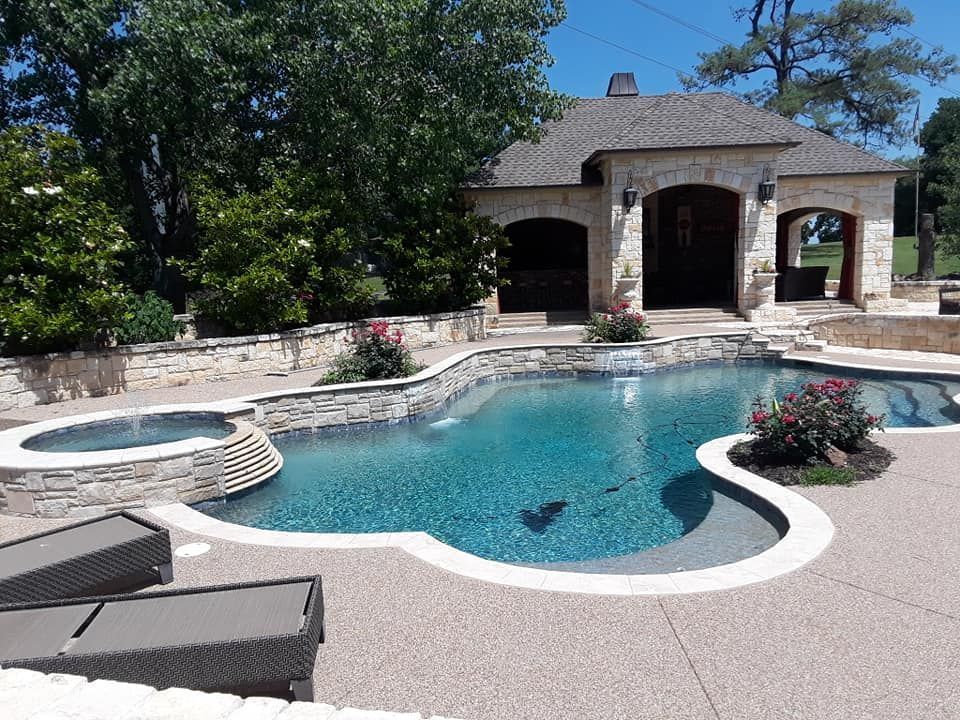 Backyard pool with hot tub, stone patio, and a shaded cabana under clear blue sky