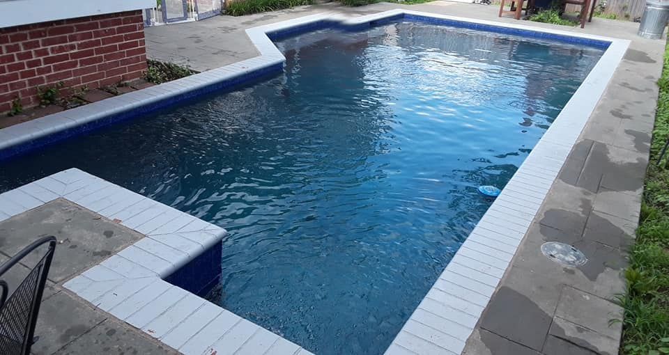 Rectangular backyard swimming pool with blue water, white tile coping, and surrounding patio paving