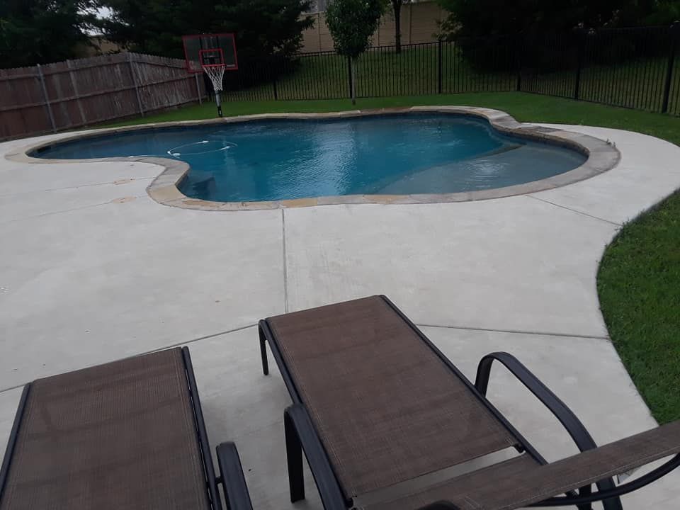 Backyard pool with two lounge chairs on a concrete patio and a basketball hoop nearby