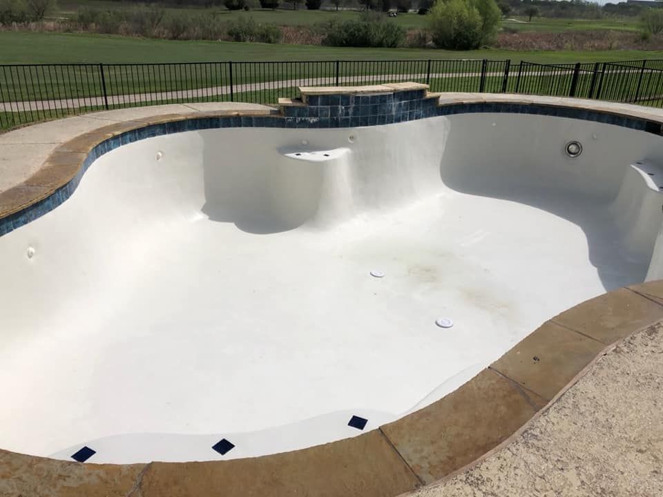 Empty white swimming pool with a tan coping edge and fence in the background